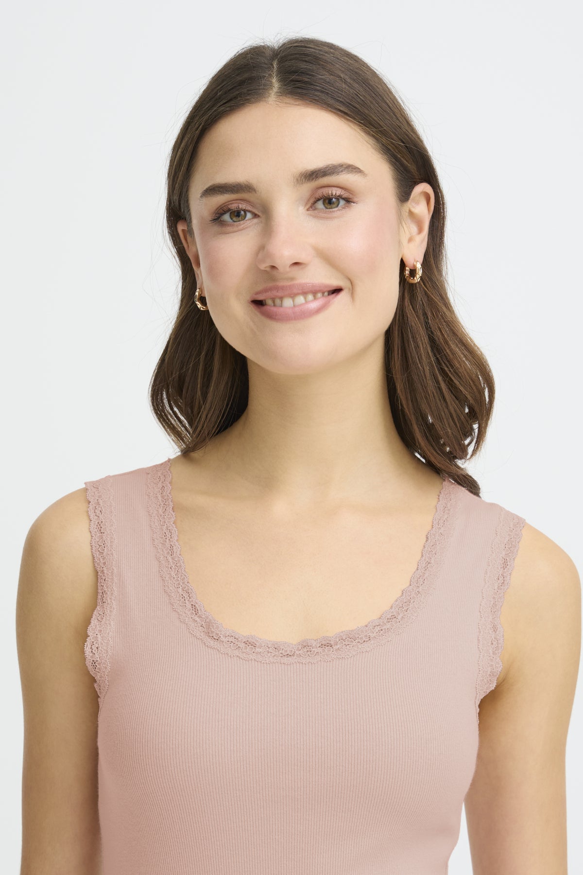 Woman wearing a light pink sleeveless top against a plain background