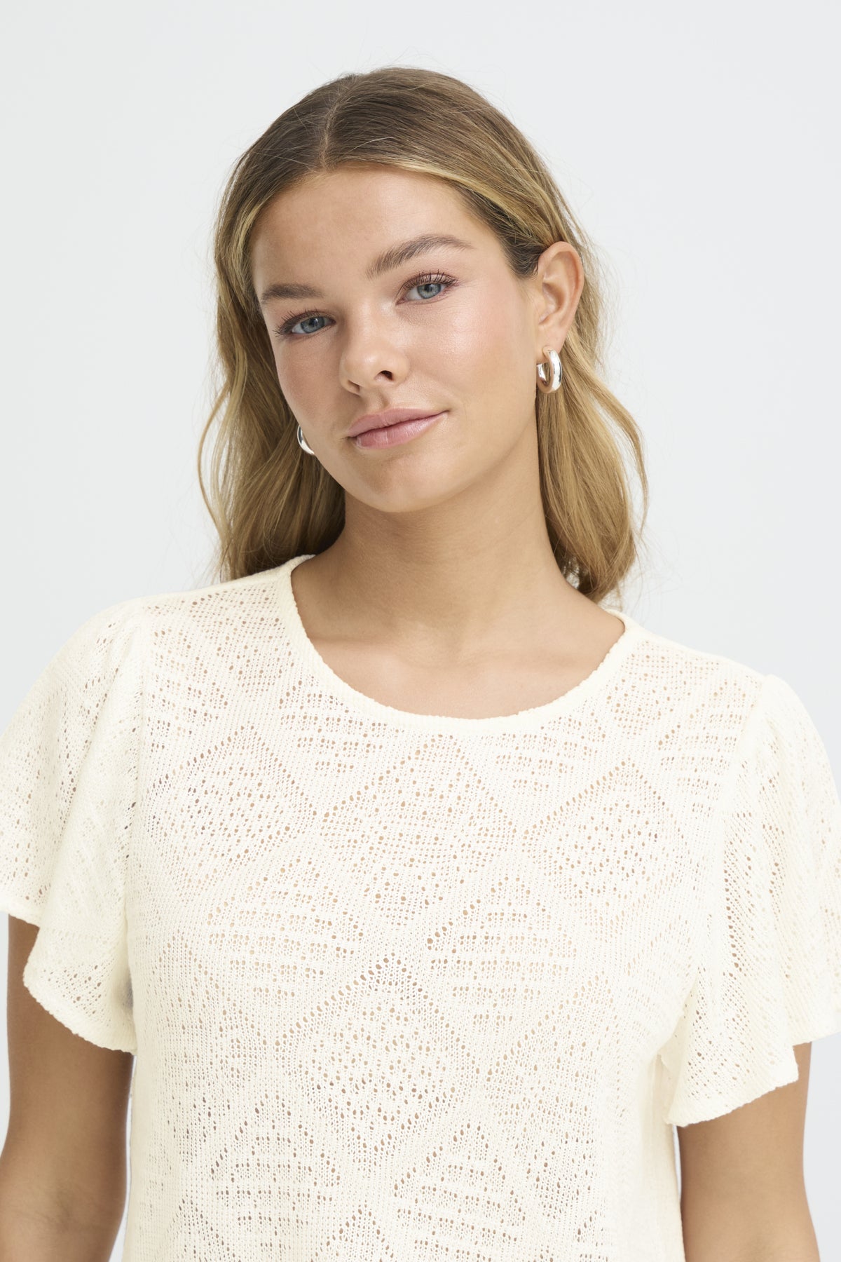 Woman wearing a textured white top against a plain background