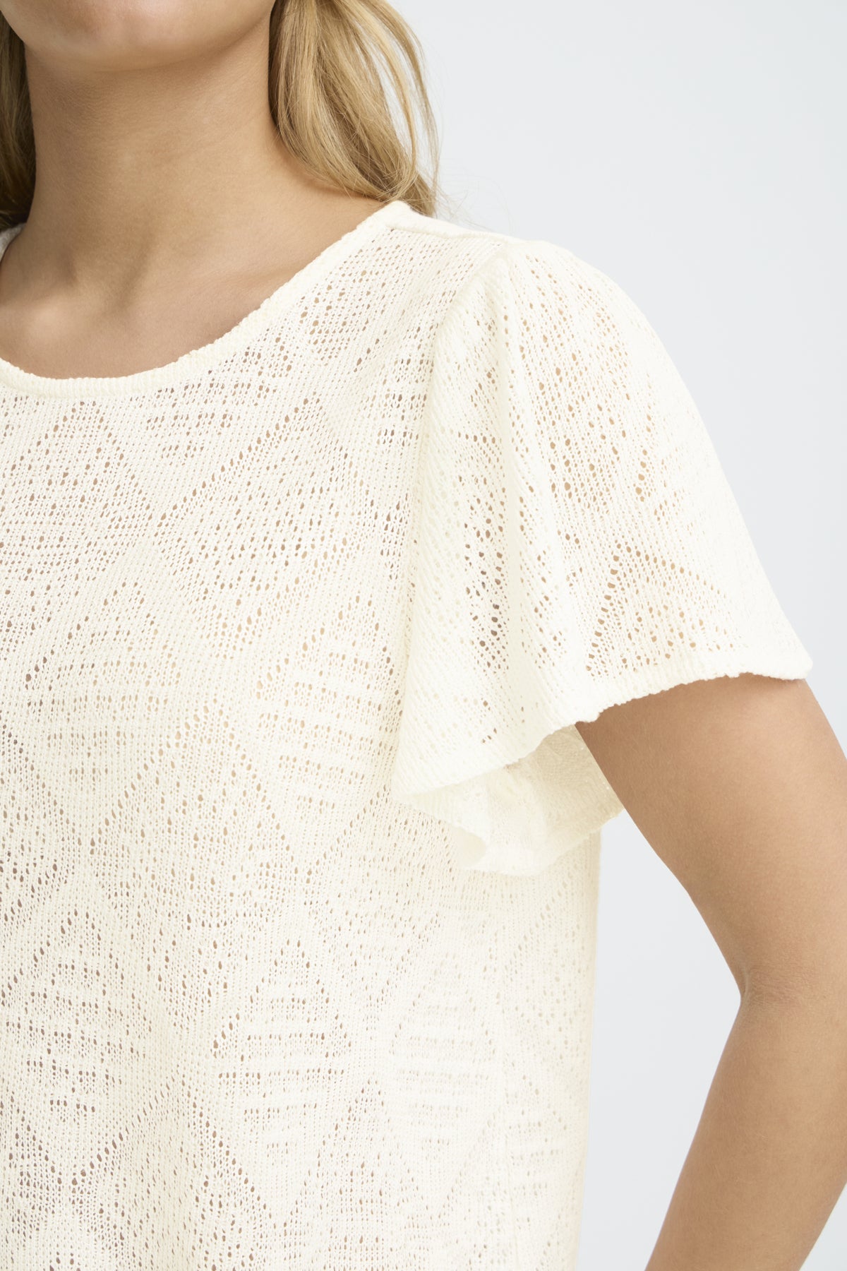 Close-up of a person wearing a textured white top against a light background