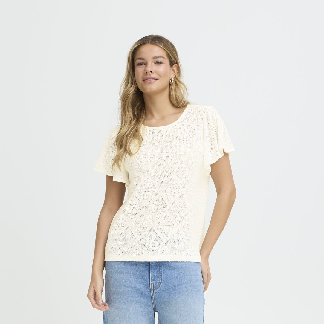 Woman wearing a white lace top and blue jeans on a plain background
