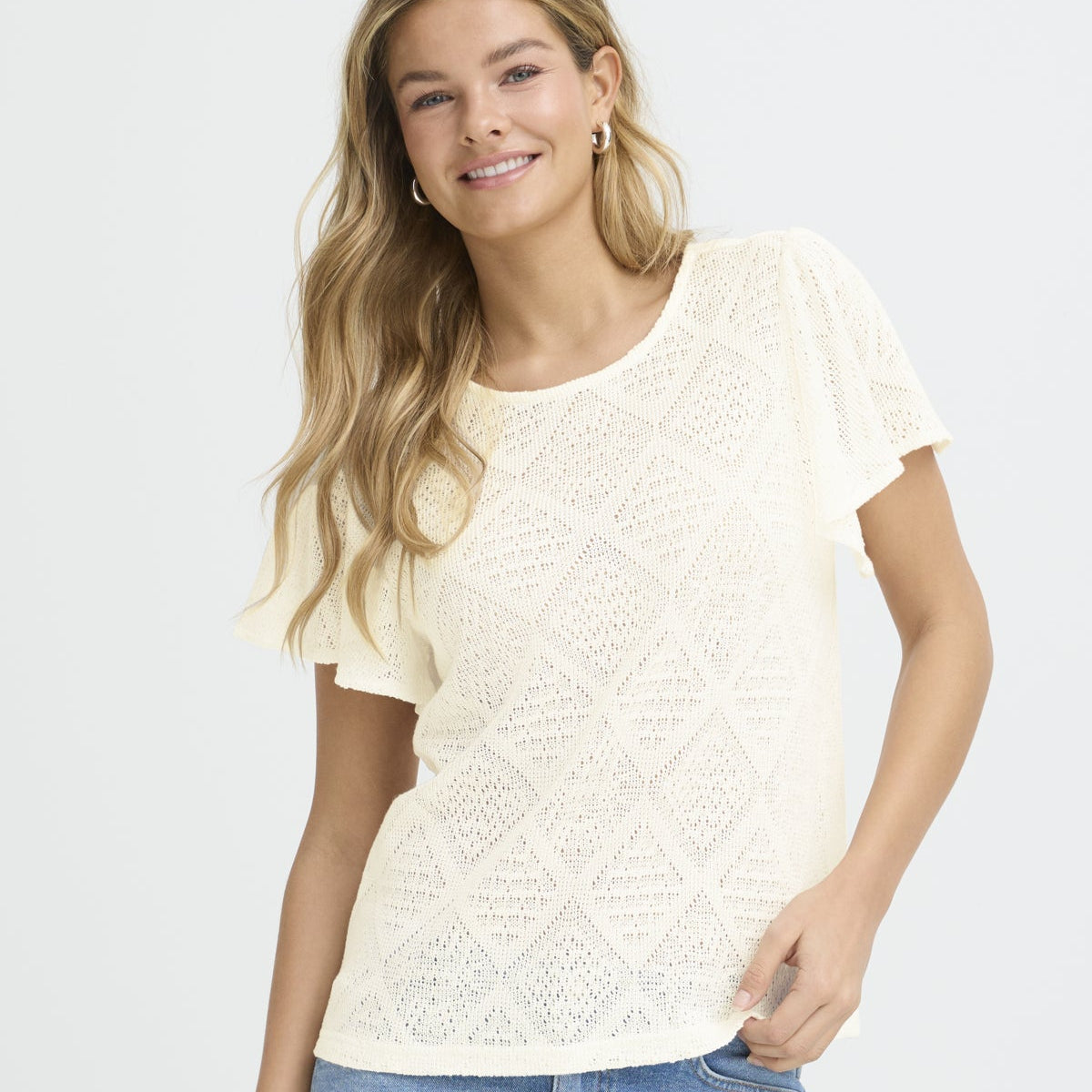 Woman wearing a white lace top and blue jeans on a white background