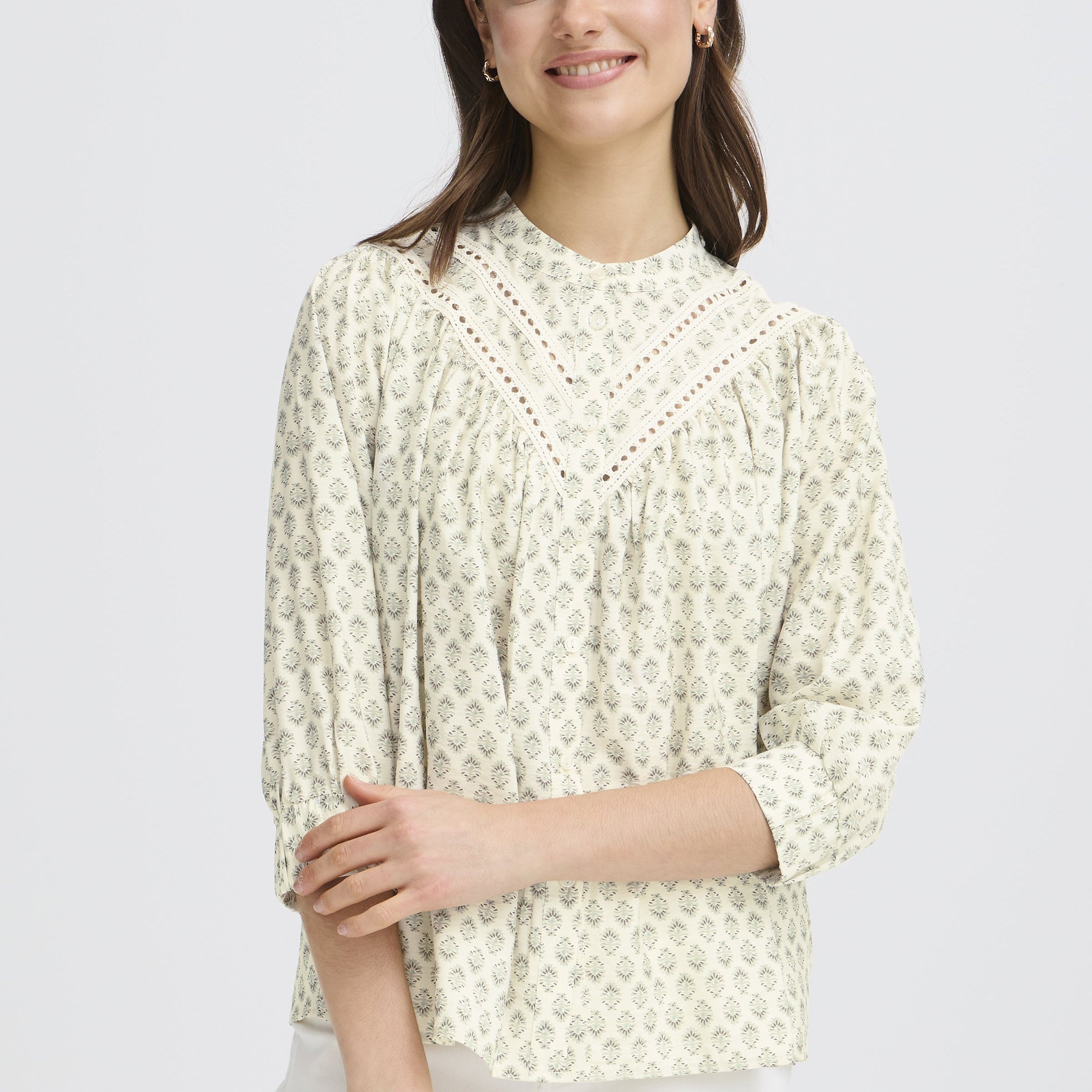 Woman wearing a light-colored lace top against a plain background