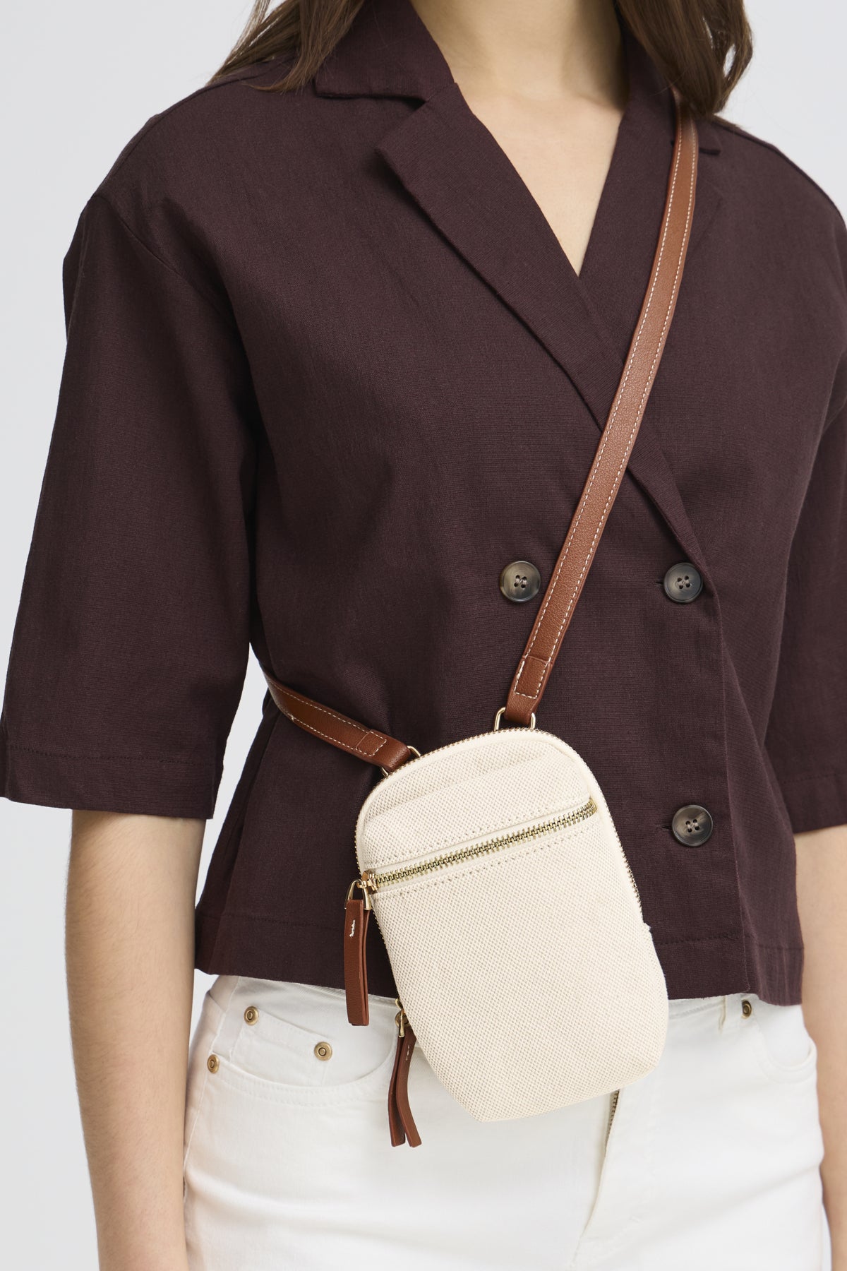 Person wearing a brown blazer with a beige crossbody bag on a white background