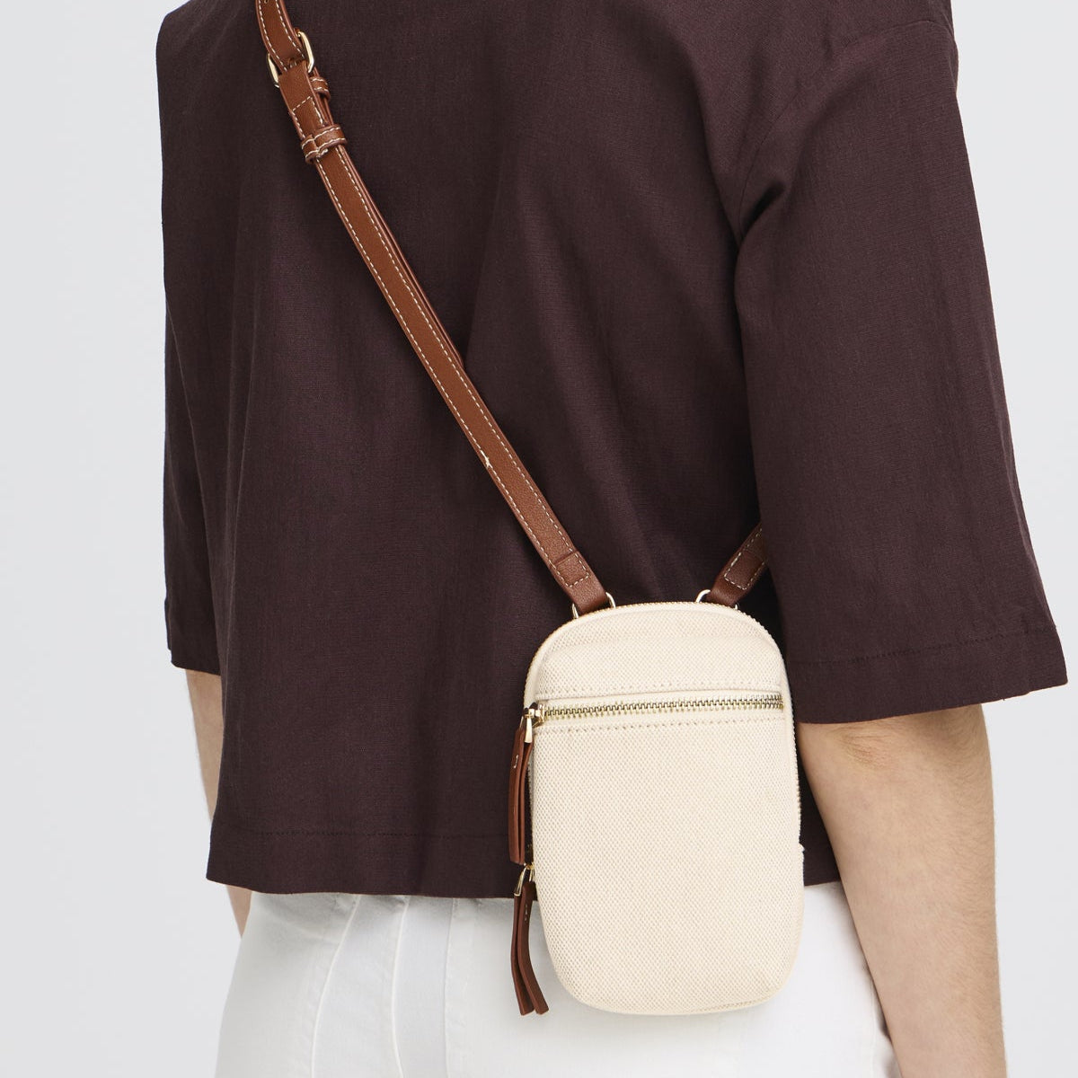 Person wearing a beige crossbody bag with a brown strap on a plain background