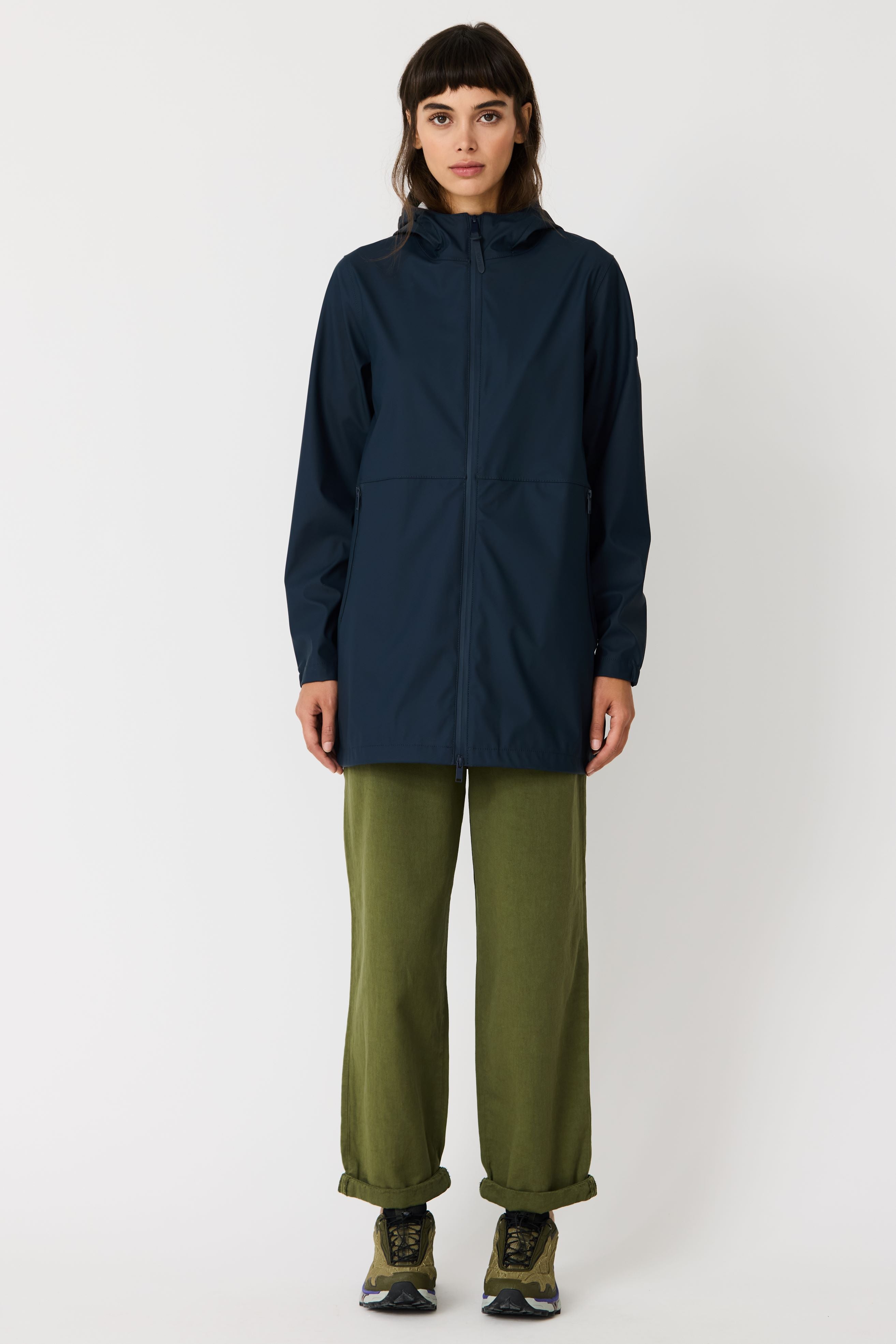Person wearing a dark blue raincoat and green pants on a white background