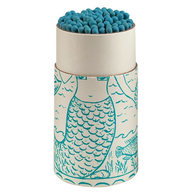 A cylindrical matchbox container with a matching lid, filled with blue matches. The container features a white base with a teal line-art illustration of a mermaid and sea life, set against a plain white background.