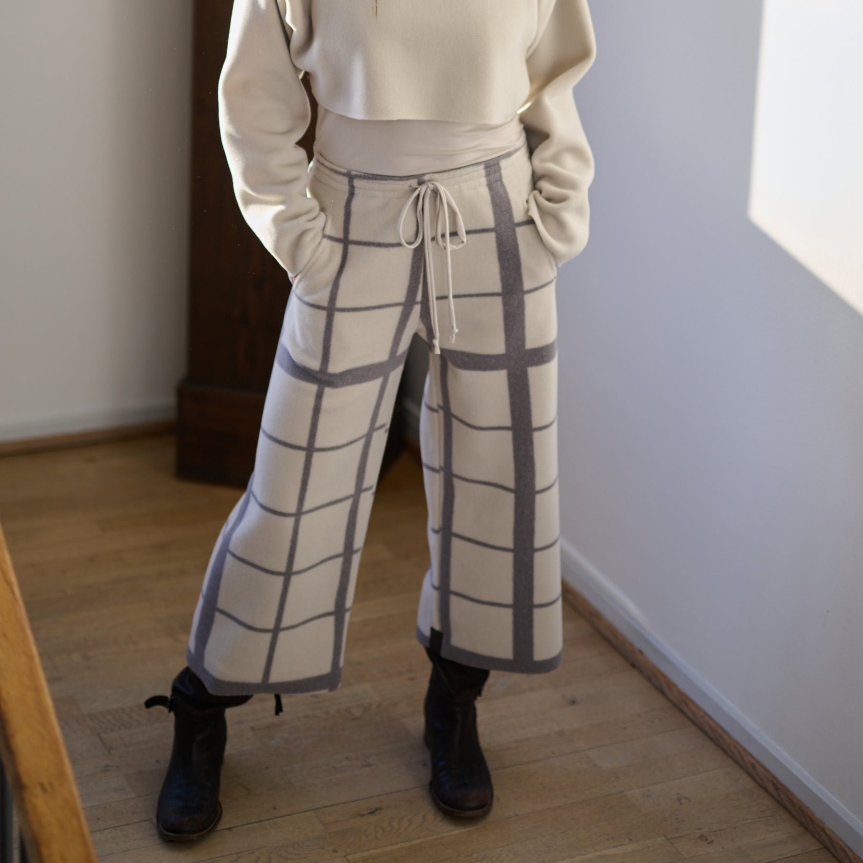 Woman wearing a beige sweater and checkered pants standing in a room with a sculpture in the background.