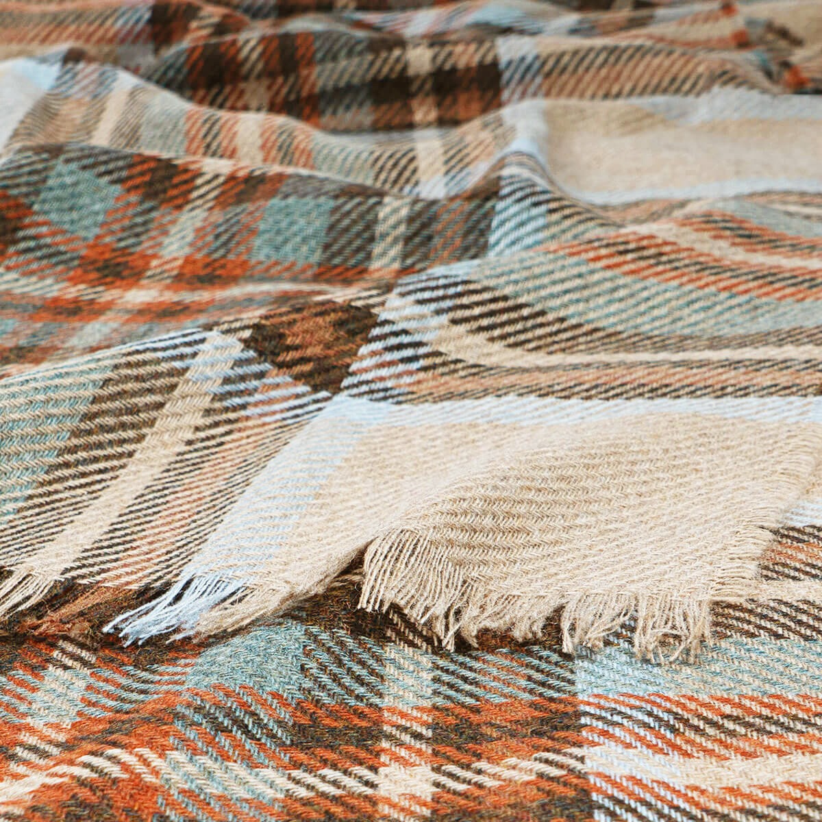 Close-up of a plaid fabric with fringes in brown, orange, and beige colors.