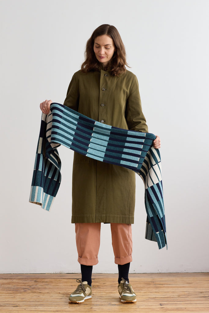 Woven throw blanket in teal, navy, and cream, featuring a geometric pattern of horizontal stripes and blocks.