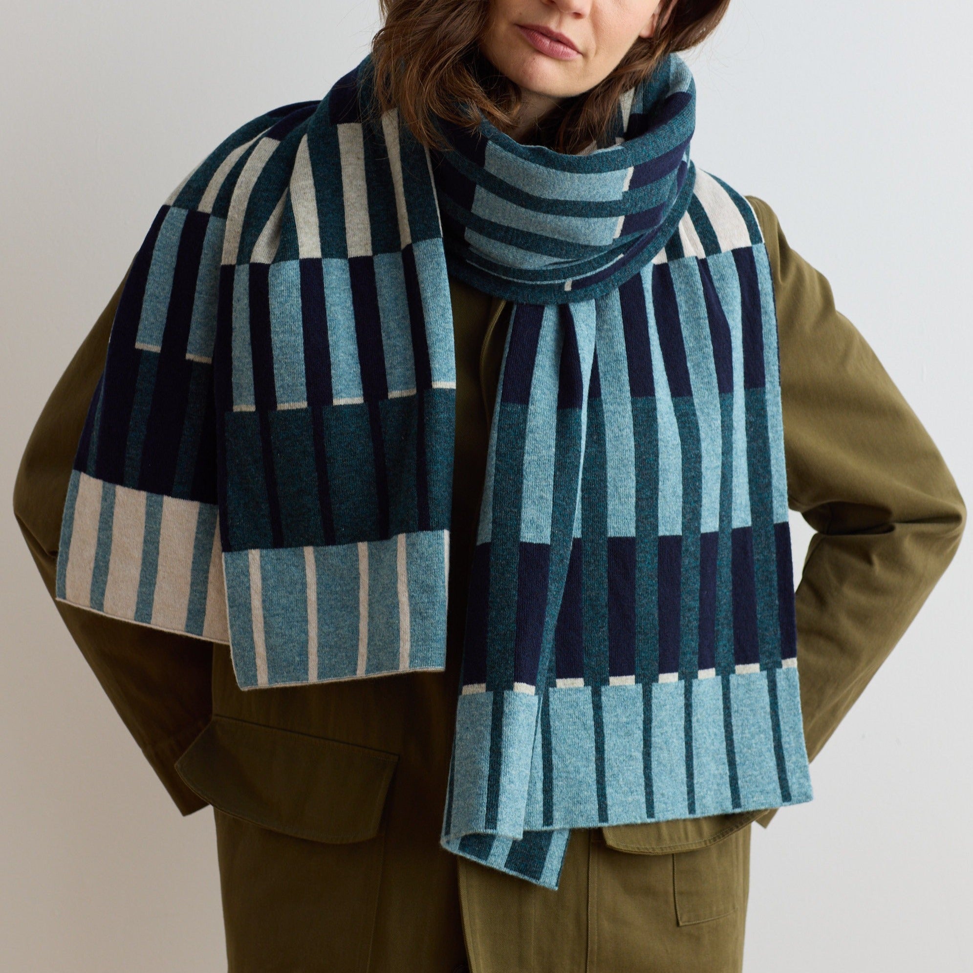 A teal, navy, and cream striped knit scarf.  The scarf features a geometric pattern of vertical stripes in varying widths.