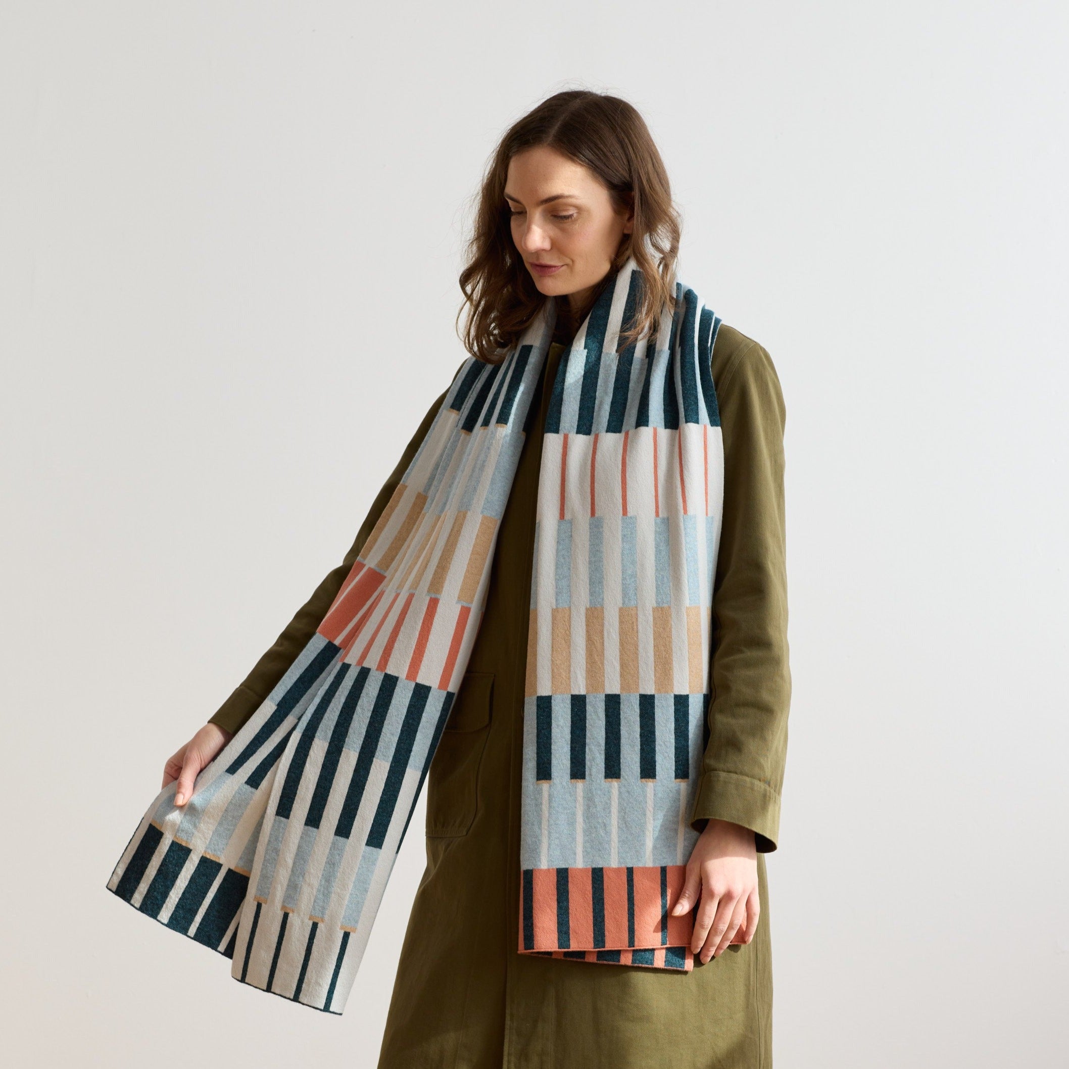 A long rectangular scarf with a geometric pattern in teal, beige, coral, and white.