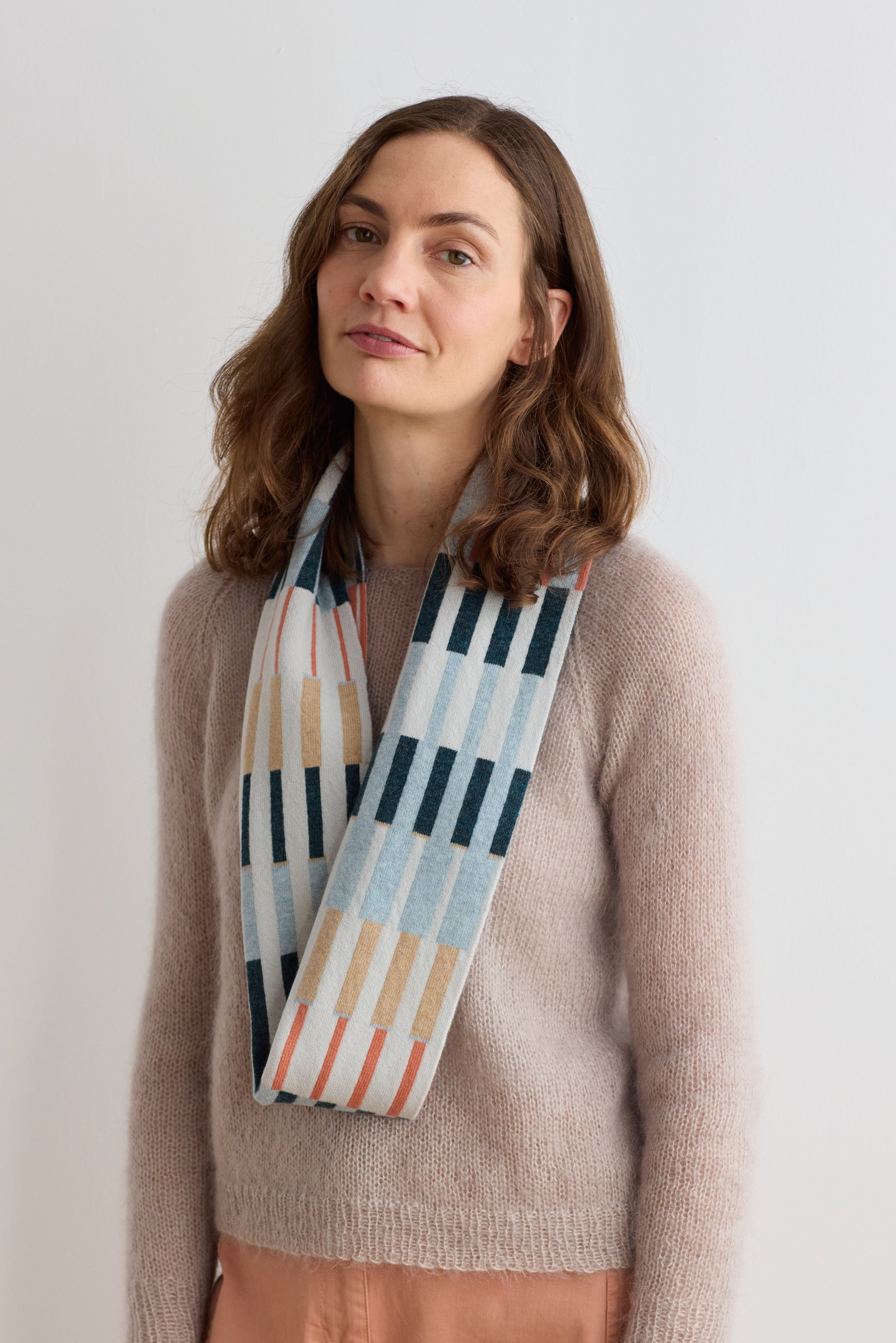 A light beige mohair sweater with a long, rectangular scarf featuring a geometric pattern of teal, peach, and beige stripes.