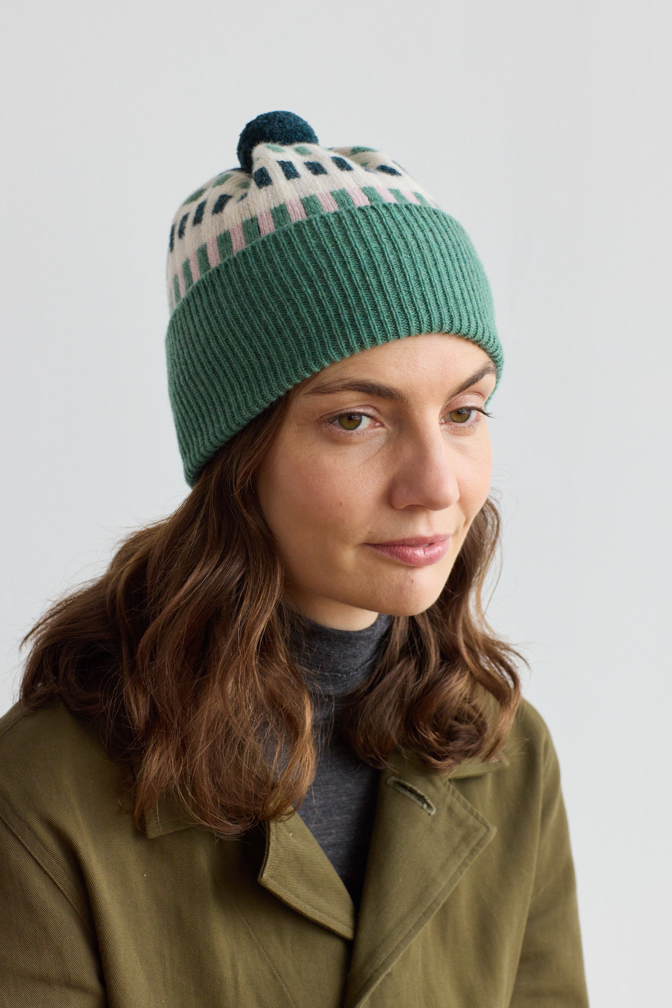 Green ribbed knit beanie with a cream and teal geometric pattern and a dark teal pompom.