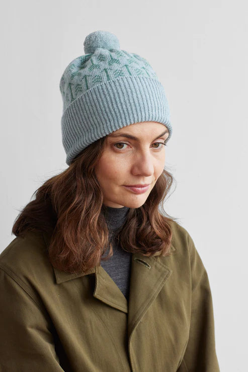 Light blue ribbed knit beanie with a pompom and subtle green patterned design.