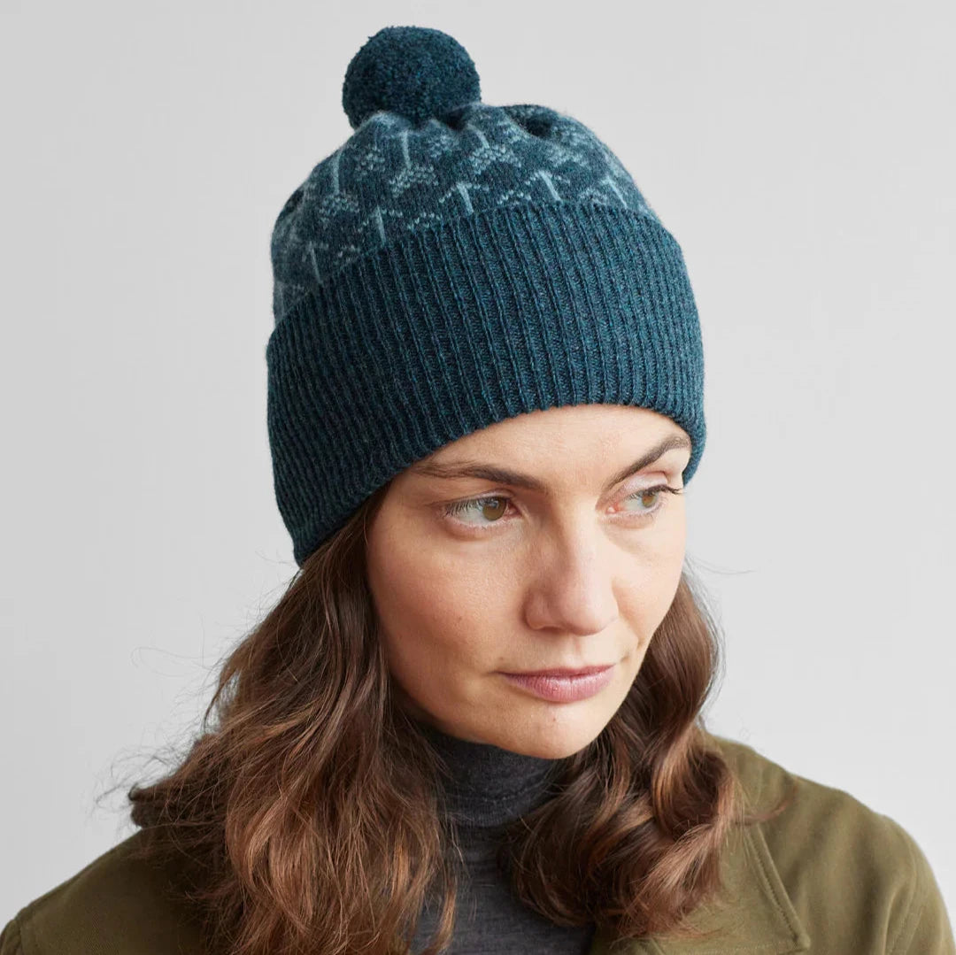 Teal ribbed knit beanie with a pompom and a Fair Isle-style pattern on the crown.