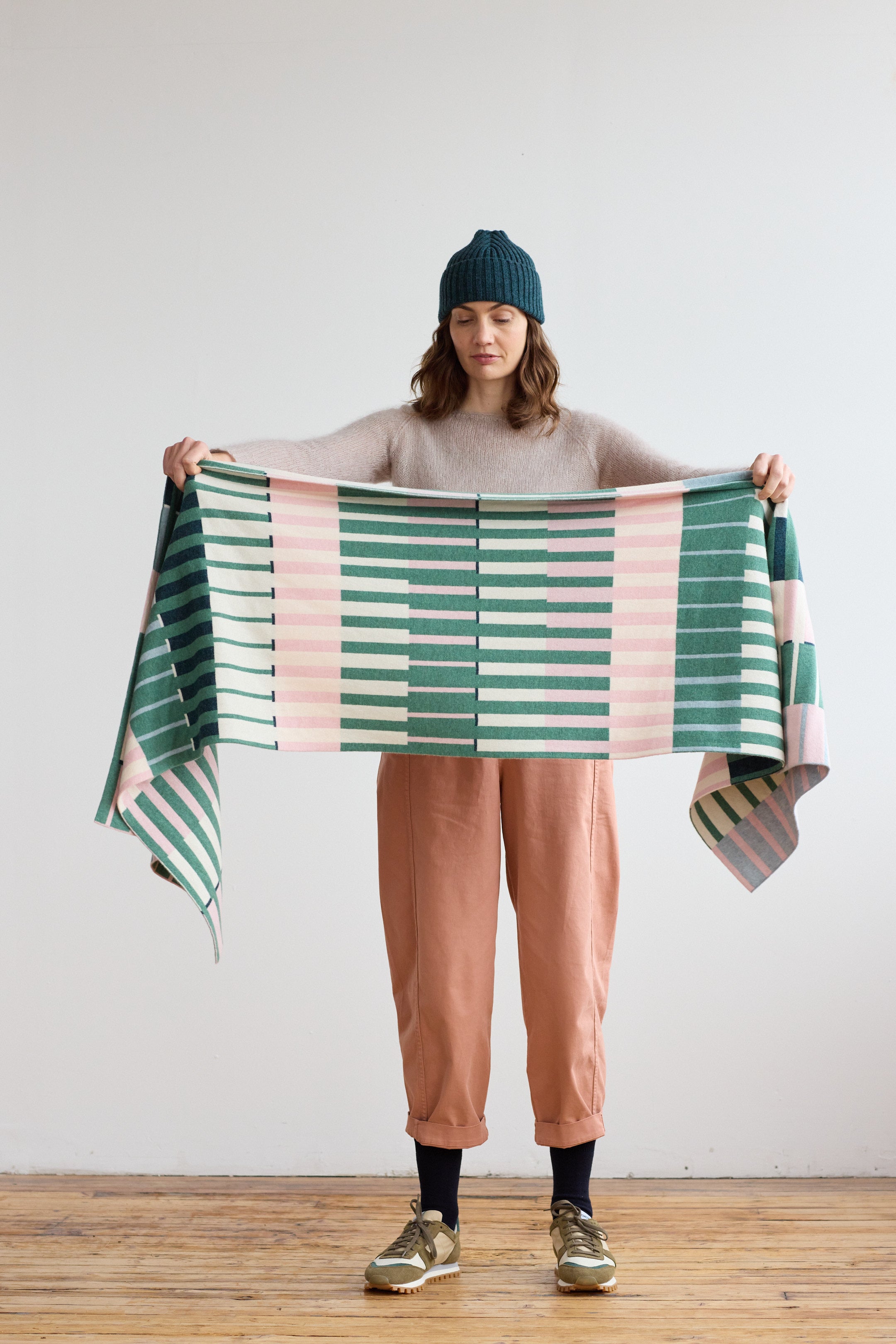 Woven throw blanket in green, pink, and cream with a horizontal striped pattern.