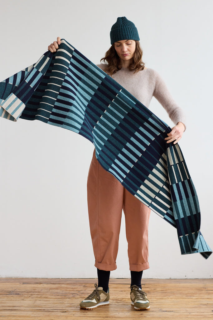 Woven throw blanket in teal, navy, and cream, featuring a geometric pattern of vertical stripes.
