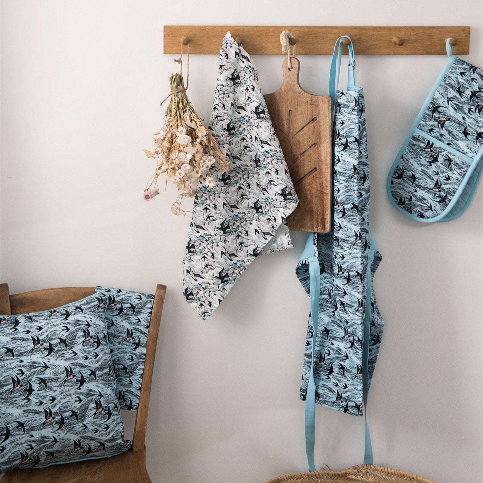 Kitchen textiles featuring a teal and black swallow print: tea towel, apron, oven mitt, and cushion covers.