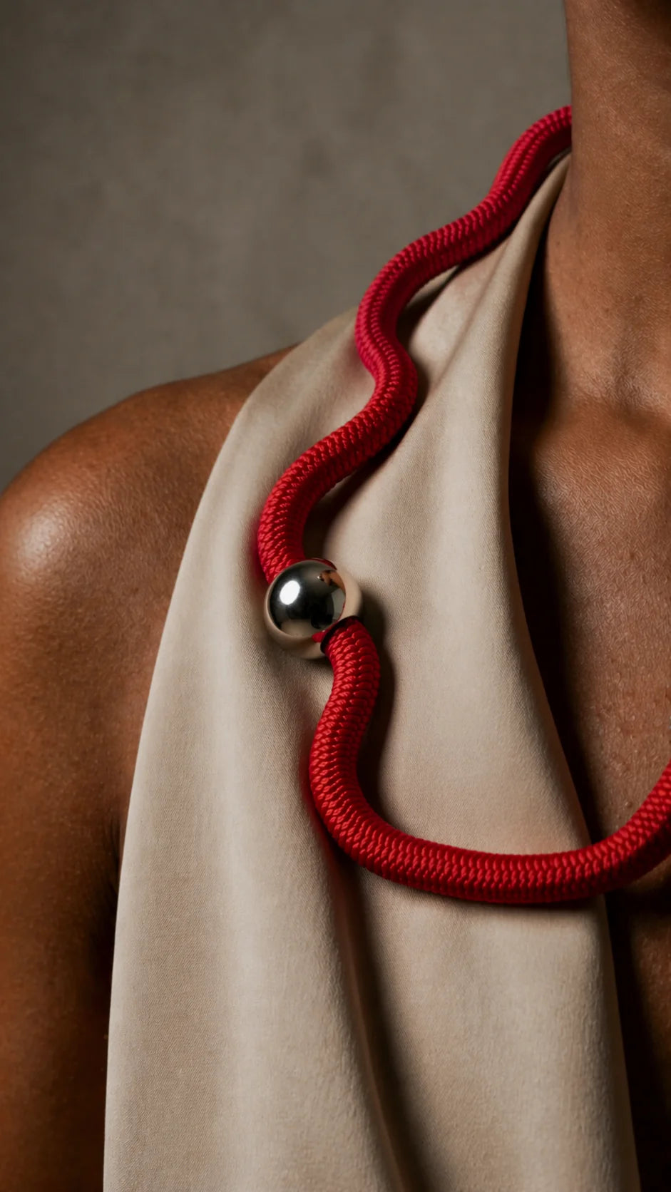 Person wearing a beige garment with a red rope and black bead detail on a neutral background