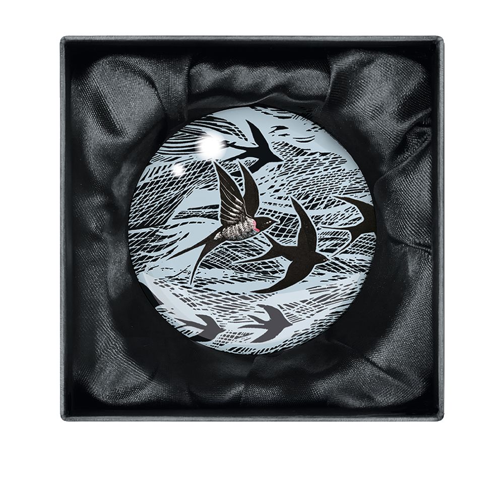 Round glass paperweight featuring a design of stylized swallows in flight against a textured background.