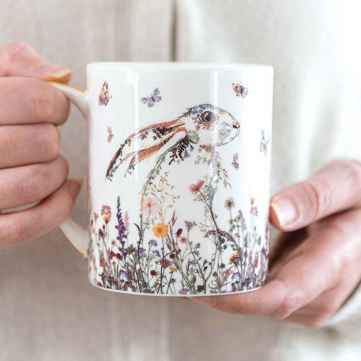 Person holding a mug with a rabbit and floral design.