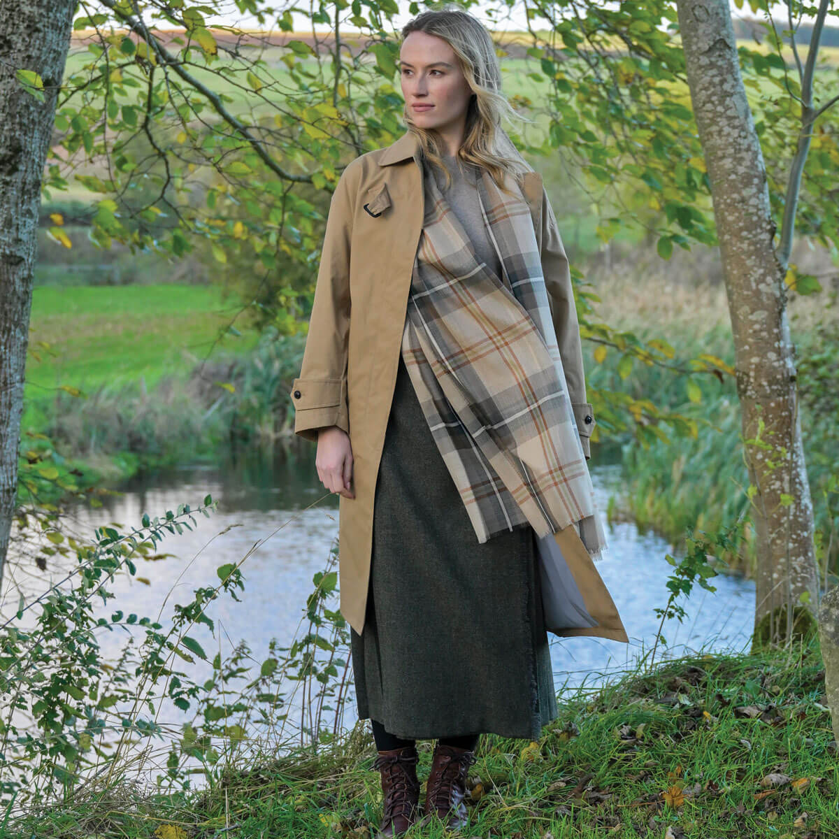 Woman standing by a pond wearing a beige coat and plaid scarf