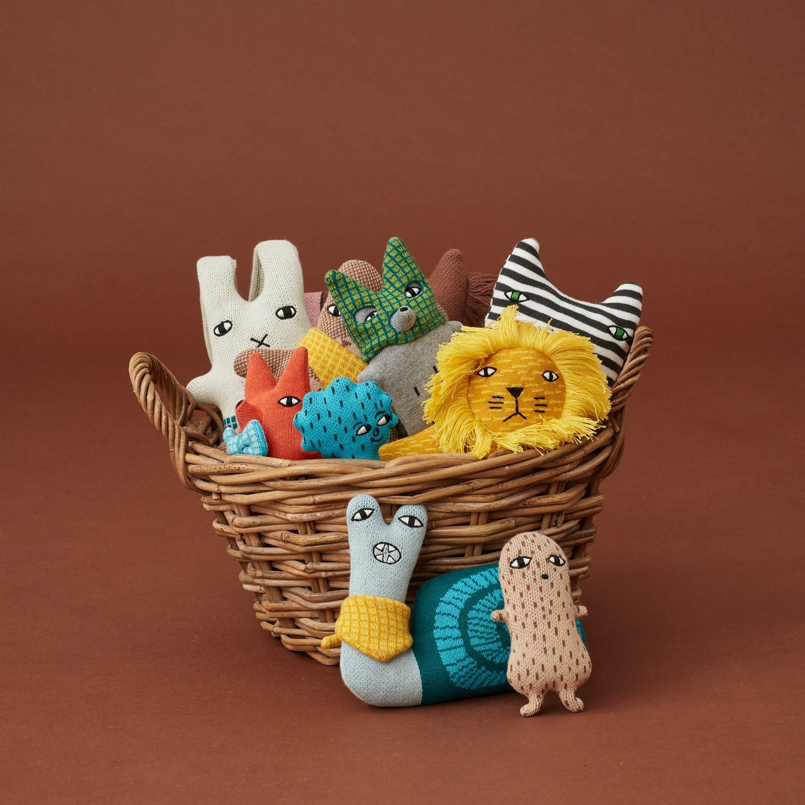 A woven basket filled with colorful plush creatures by Donna Wilson, featuring yellow, orange, green, and blue shades.