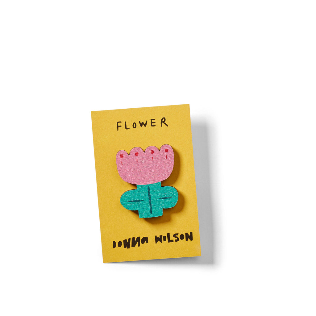 A colorful flower brooch with a pink top and green leaves on a yellow card, labeled "Donna Wilson."