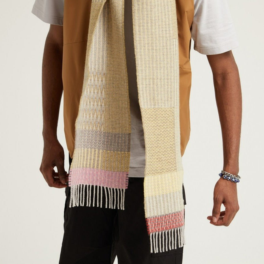 Woven wool scarf in pale yellow, gray, and pink with fringed edges.
