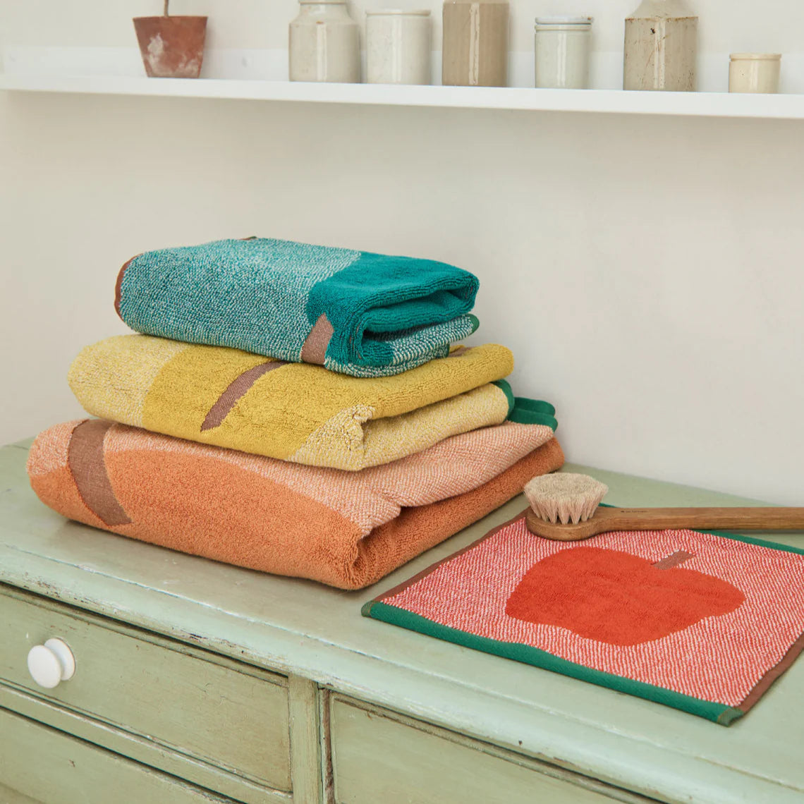 Stack of colorful towels on a wooden surface with a pumpkin-themed mat.