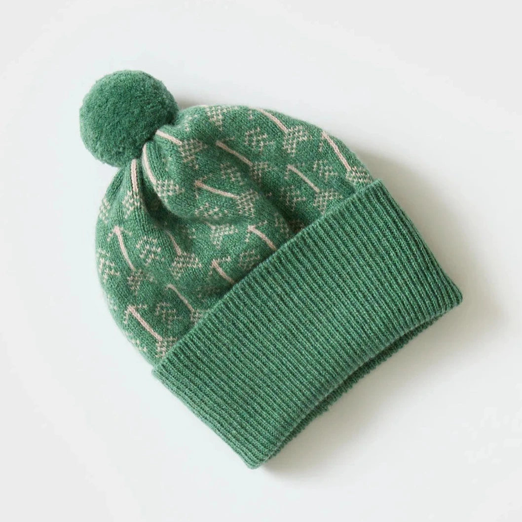 Green knit beanie with a pompom and a subtle cream-colored arrow pattern.