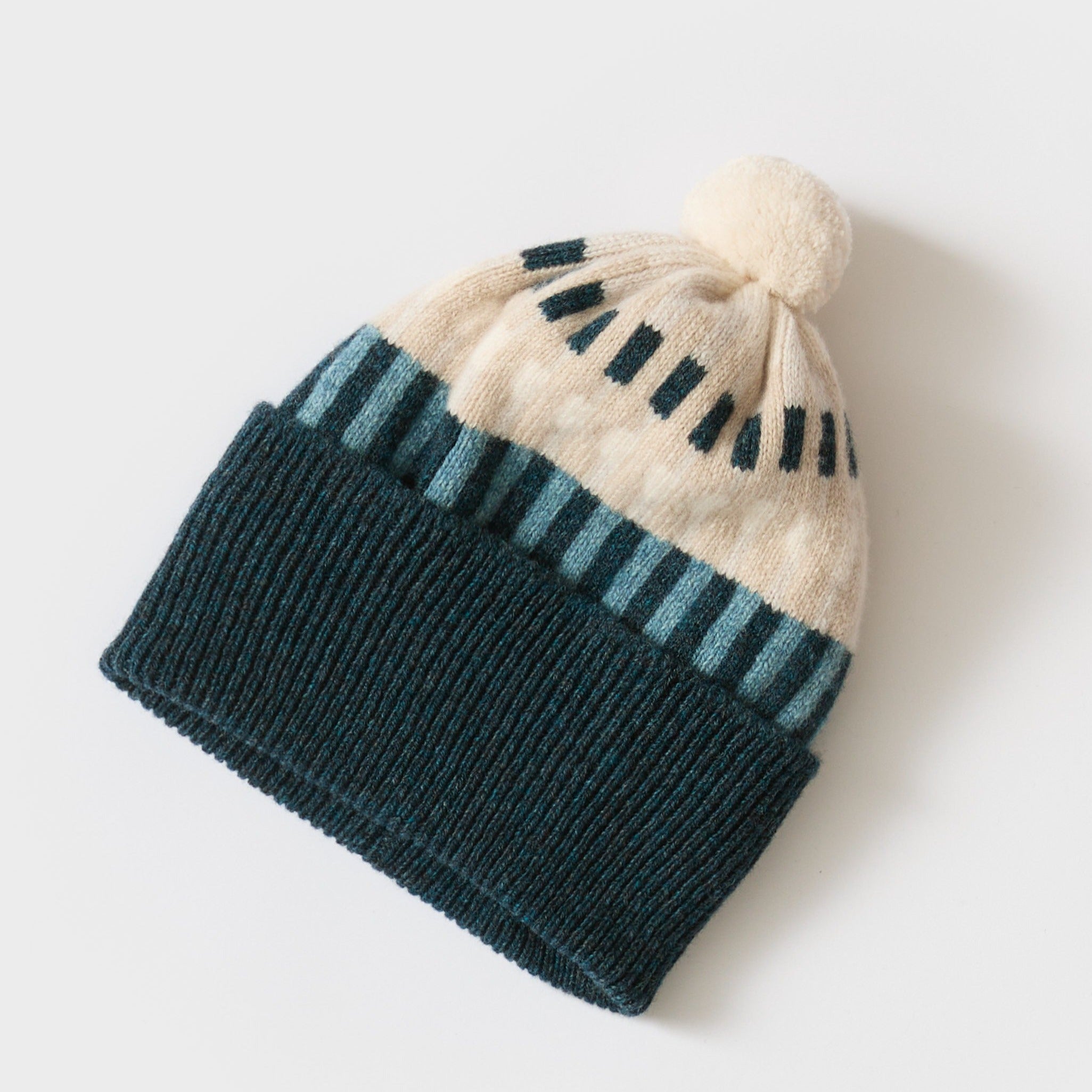 Knit beanie with teal and cream striped pattern, featuring a cream pompom.
