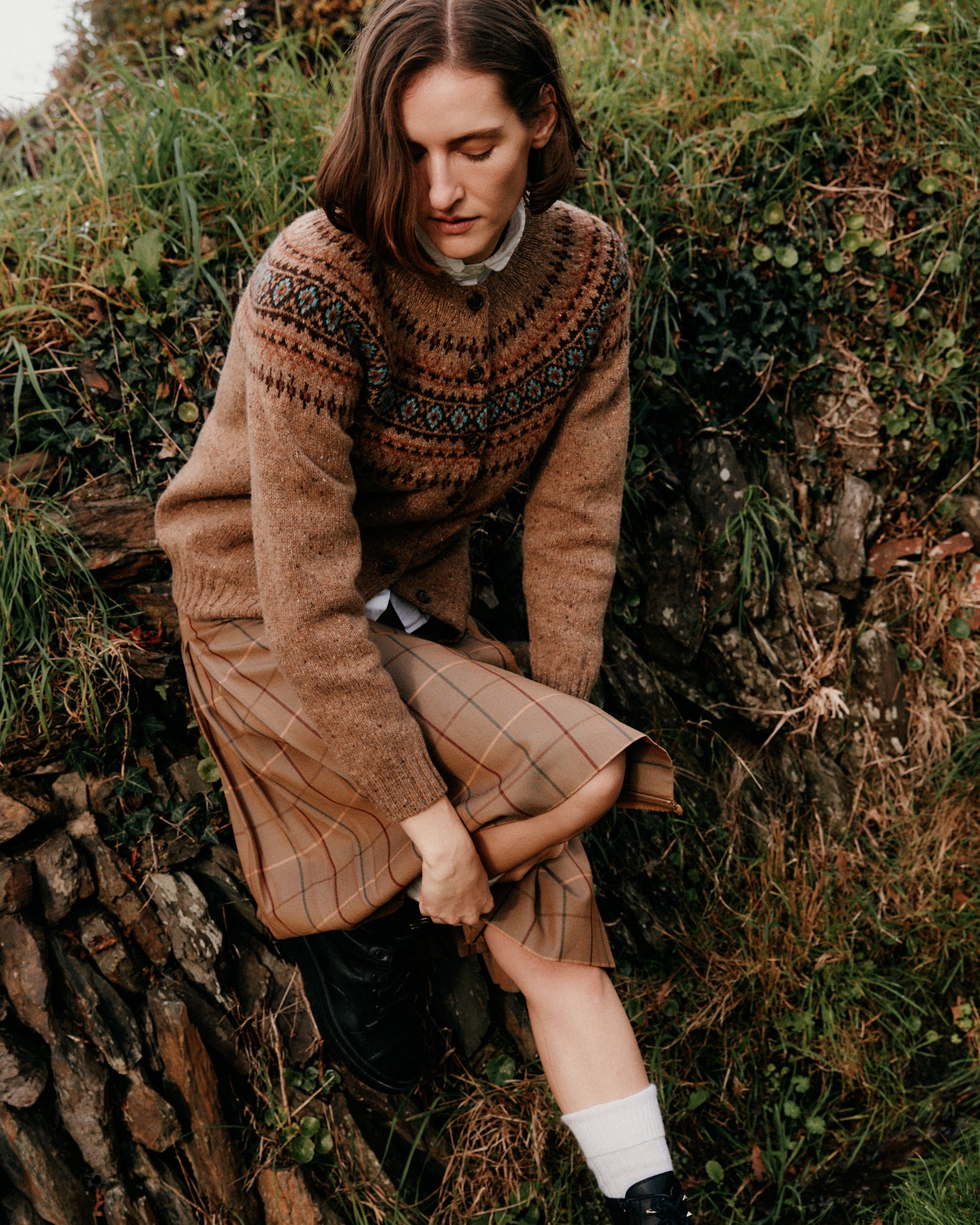 Woman in a patterned sweater sitting on a stone wall in a natural setting