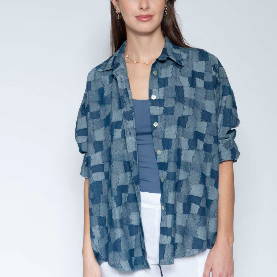 Woman wearing a blue patterned shirt over a blue top and white pants on a light gray background