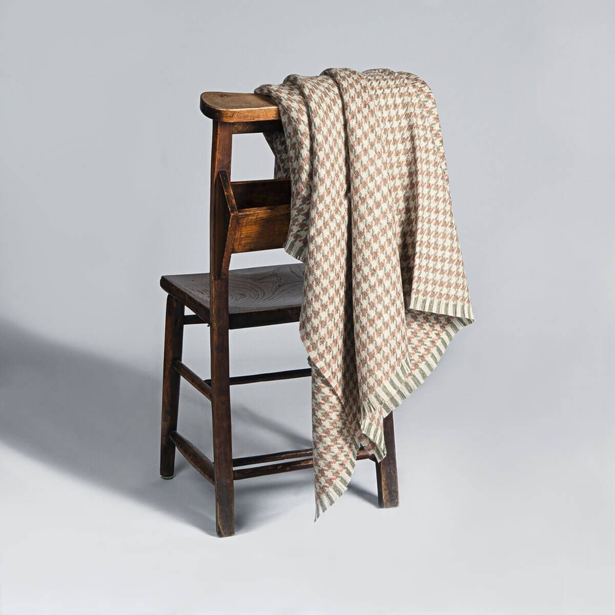 A beige and brown houndstooth throw blanket draped over a dark wooden chair.