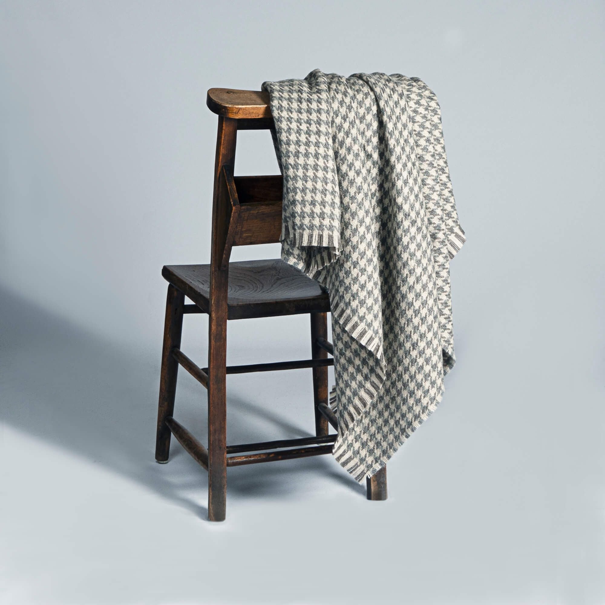 Grey and beige houndstooth throw blanket draped over a dark wooden chair.