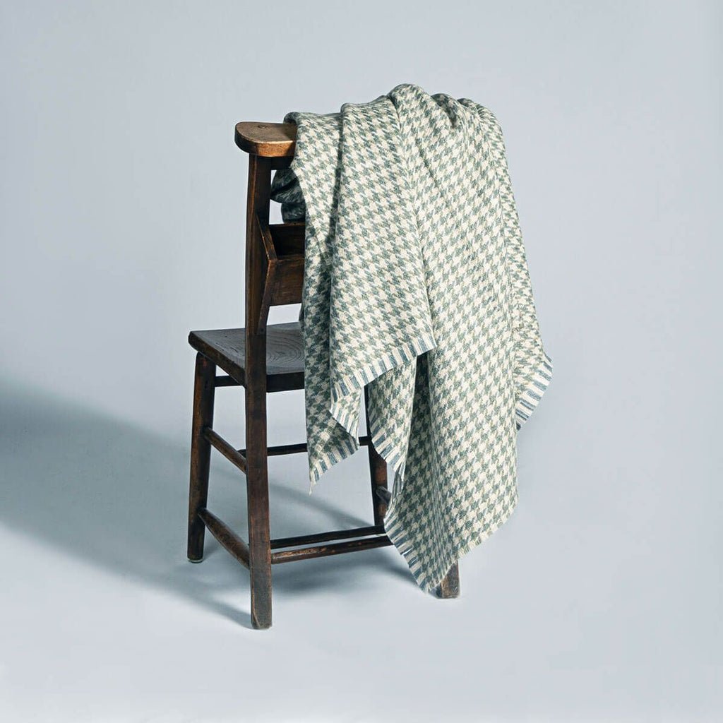 A light grey and green houndstooth throw draped over a wooden chair.