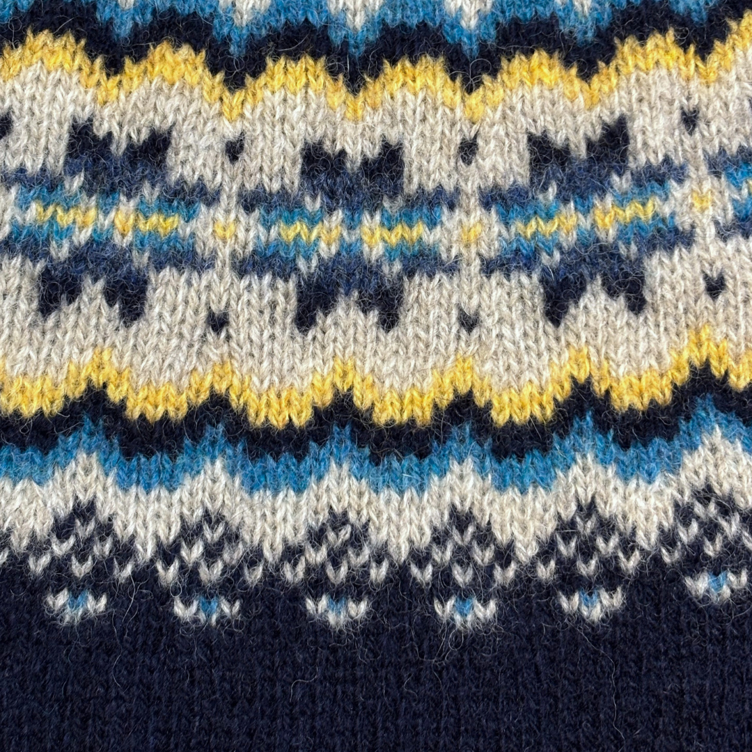 Close-up of hand-knitted wool fabric with a Fair Isle pattern in navy, beige, light blue, and yellow.