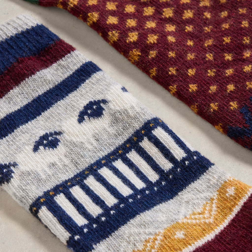 Pair of wool socks with intricate patterned designs; one sock features a grey base with navy and gold details, the other a