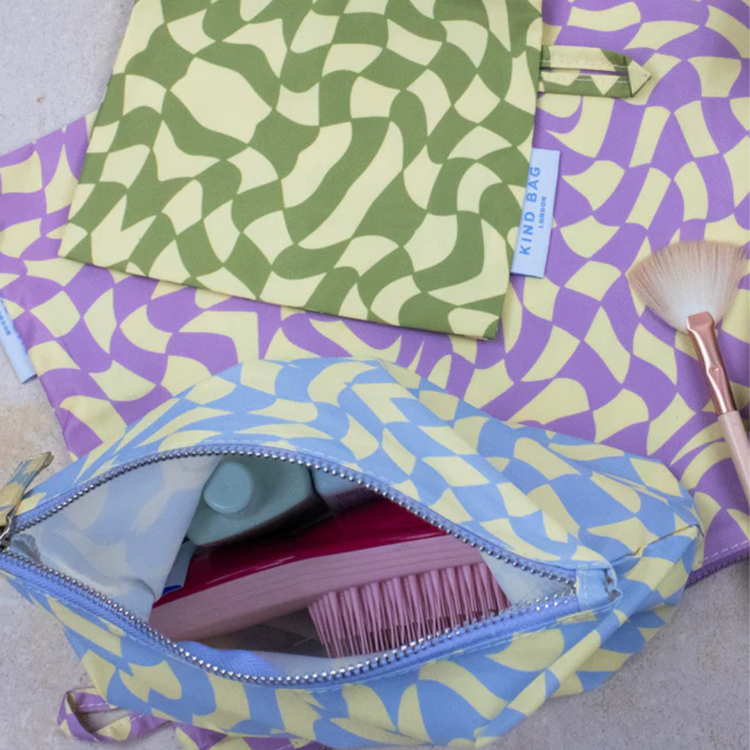 Light blue wash bag with yellow and purple abstract pattern, open to reveal toiletries including a hairbrush.