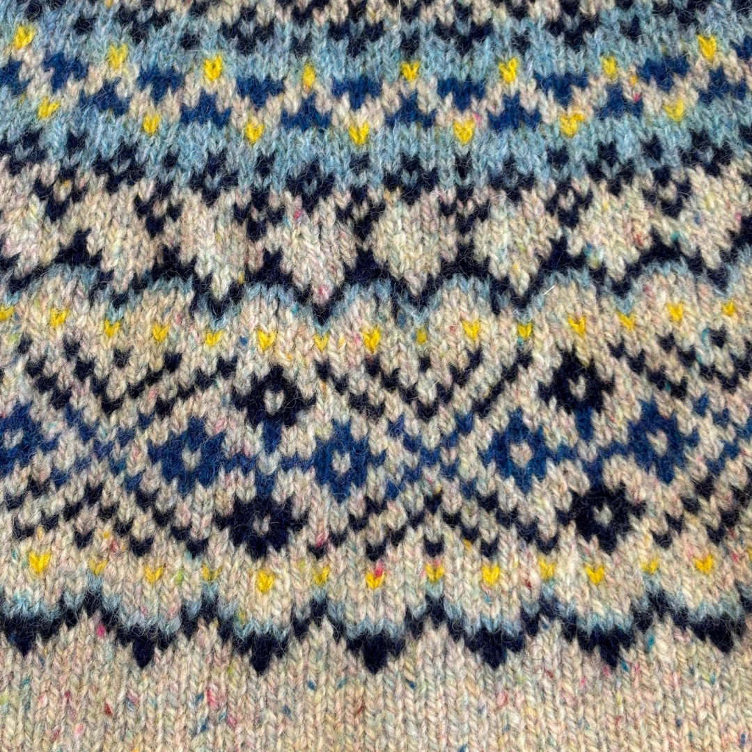 Hand-knitted wool fabric with a Fair Isle pattern in shades of blue, beige, and black, accented with yellow.