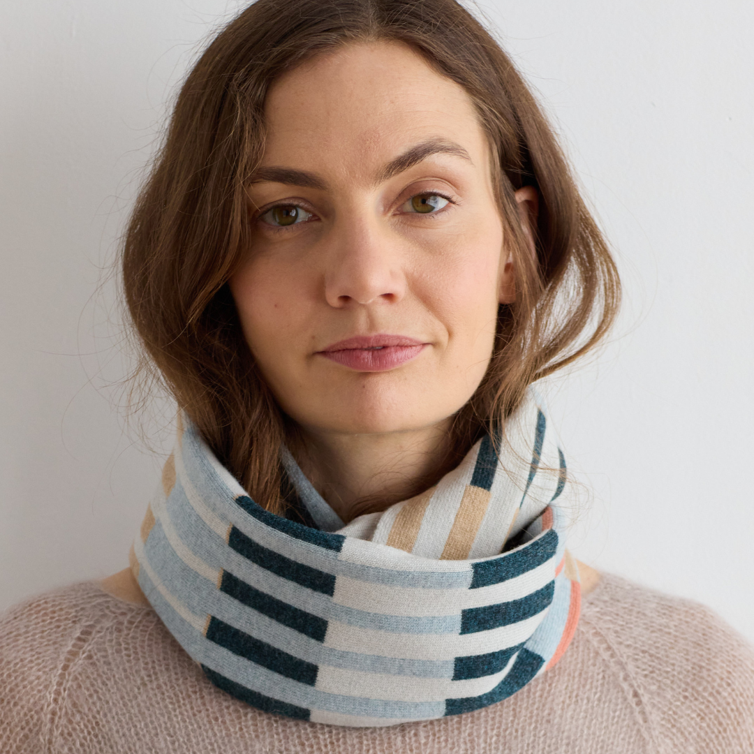 A soft, folded neck warmer with a geometric pattern in shades of blue, beige, and coral.