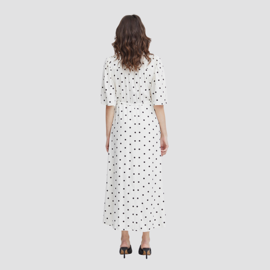 A woman wearing a white Fransa dress with black polka dots, seen from the back, paired with black heels.