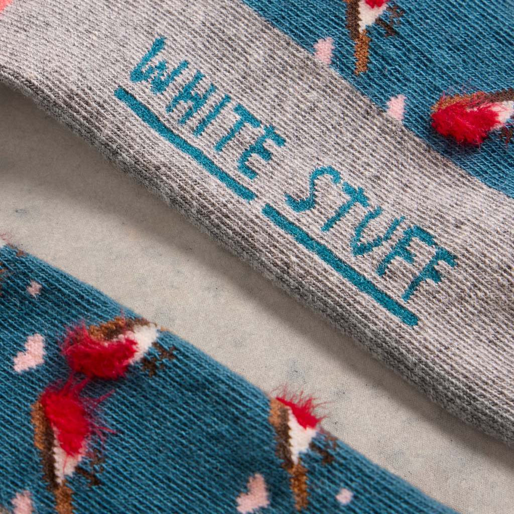 Close-up of a pair of White Stuff socks; teal with a bird pattern and a grey band displaying the brand name.