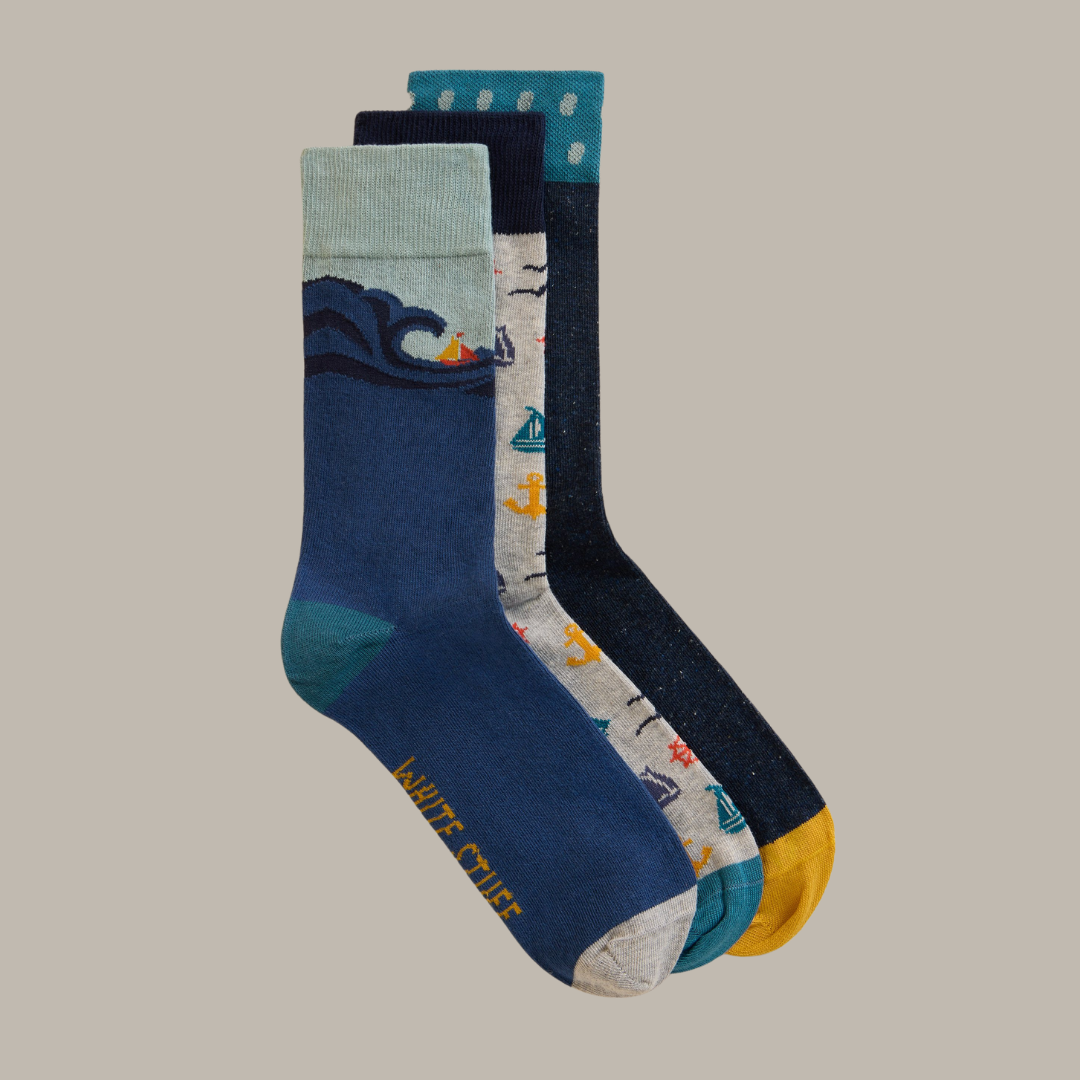 Three pairs of men's crew socks; navy blue with wave and sailboat design, light grey with anchors and sailboats, and dark