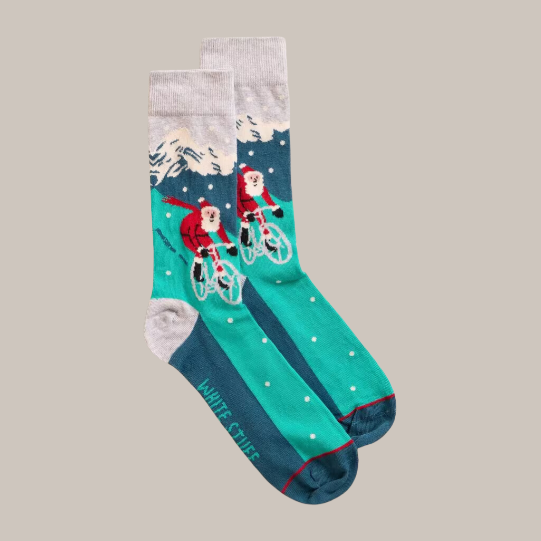 Pair of teal Christmas socks featuring Santa Claus riding a bicycle in a snowy mountain scene.