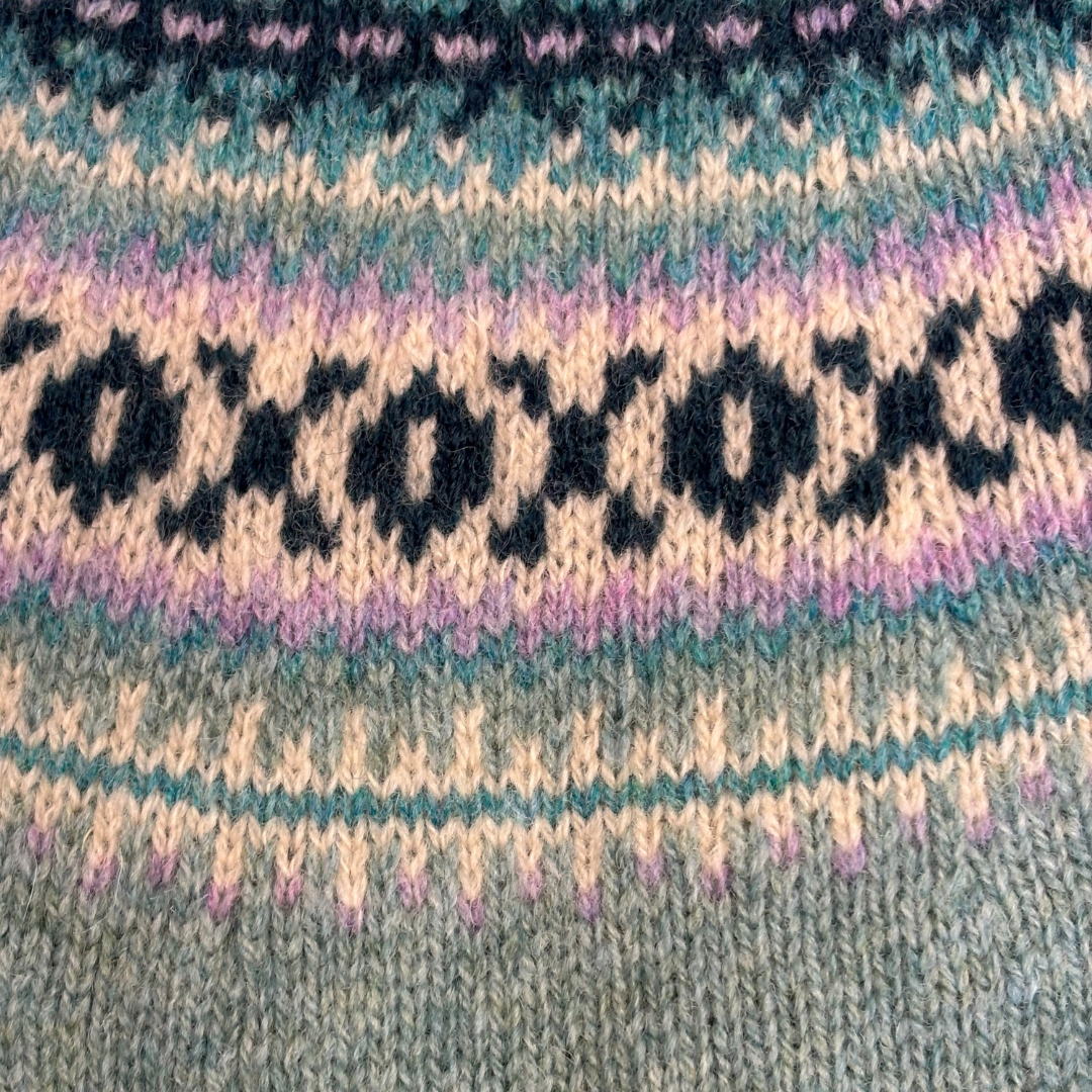 Close-up of a knitted fabric with a Fair Isle pattern featuring a repeating text motif in dark yarn against a lighter