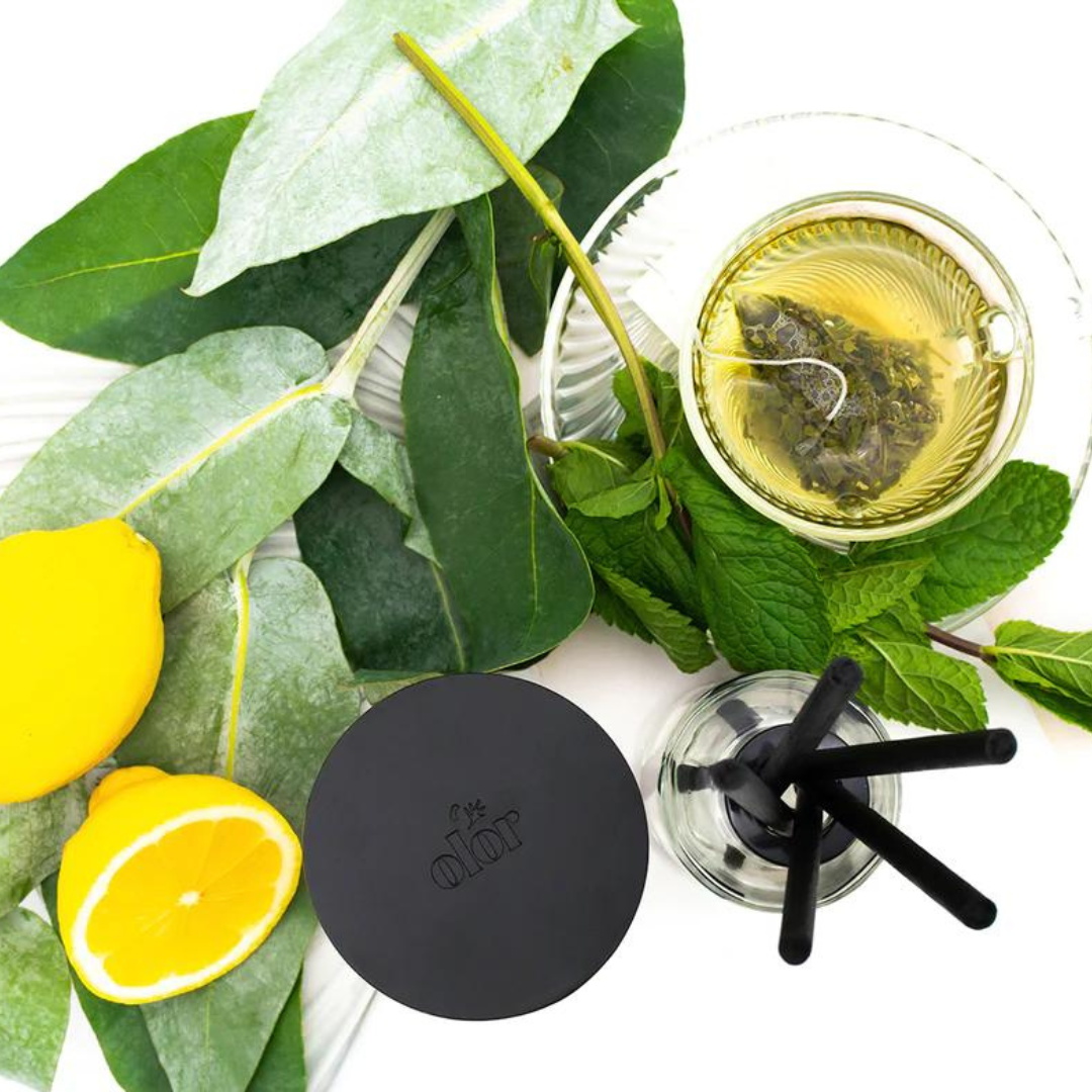 Black diffuser base with black reeds,  accompanied by lemons, mint, and eucalyptus leaves.
