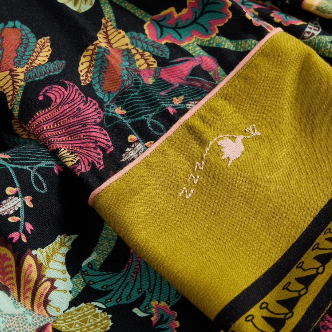 Close-up of a garment's cuff, featuring a dark floral print and a contrasting mustard yellow fabric section with embroidered