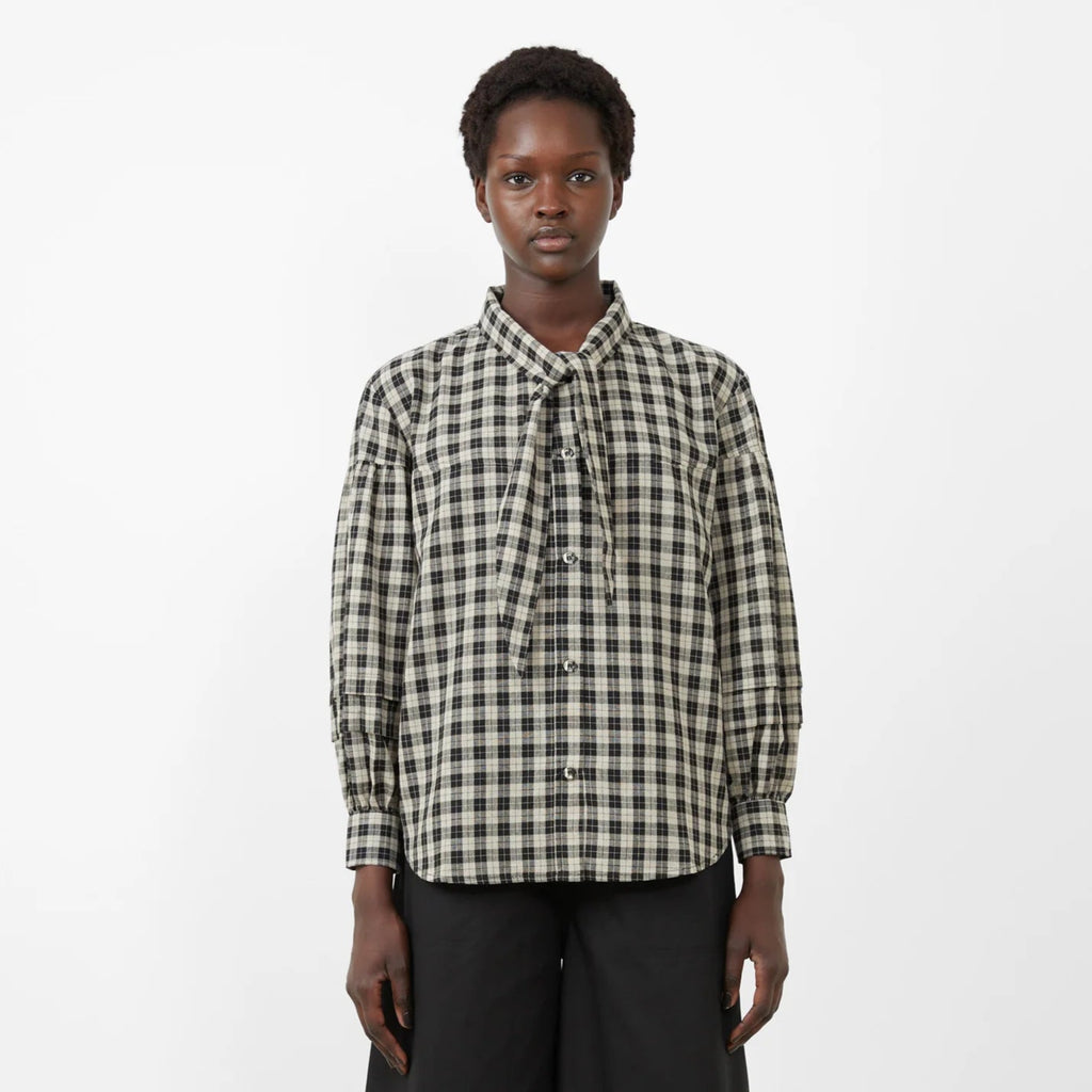 Person wearing a checkered shirt and black wide-leg pants on a white background